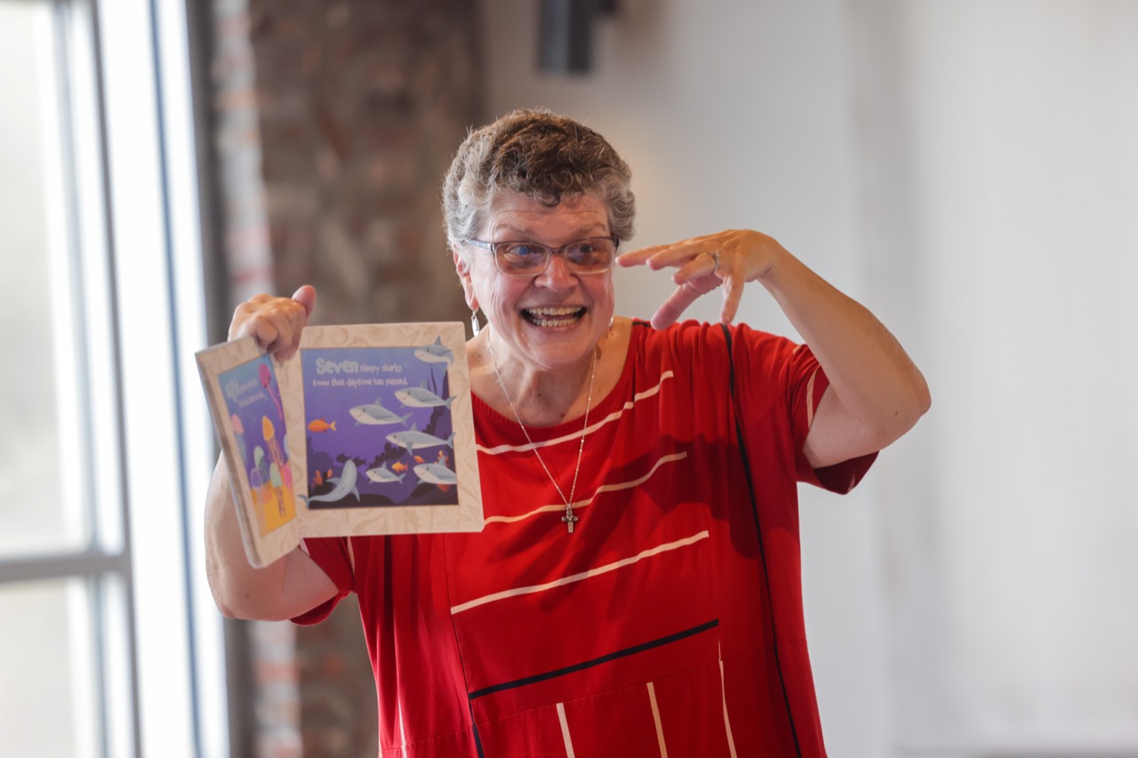 Hope Taylor Spencer smiling as she reads a colorful children’s book aloud